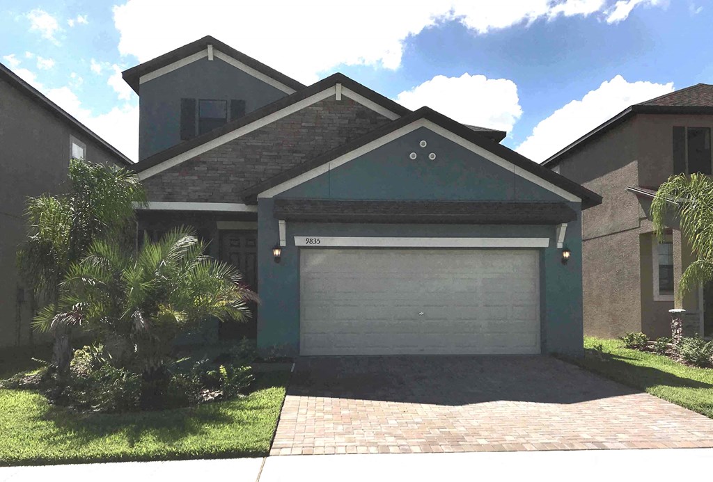 A house with a grey garage door and a brick driveway.
