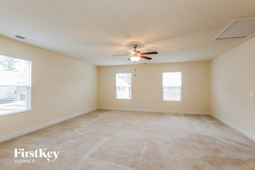 A spacious room with a ceiling fan and two windows.