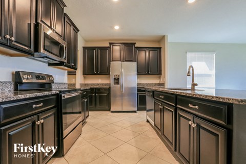 A kitchen with black cabinets and a stainless steel refrigerator.