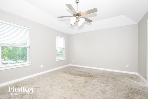 A spacious room with a ceiling fan and two windows.
