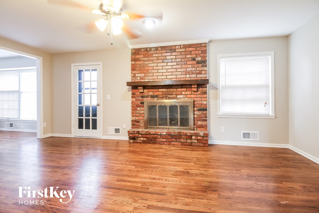 an empty living room with a brick fireplace and wooden floors