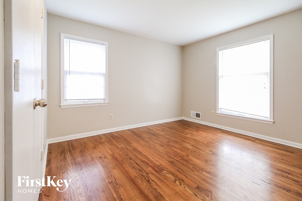 an empty room with wood floors and two windows