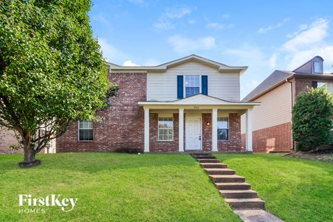 A house with a white front porch and a tree in front of it.