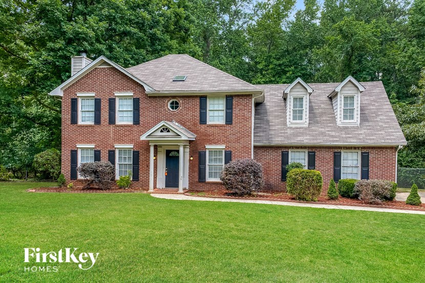 a brick house with a green lawn and trees