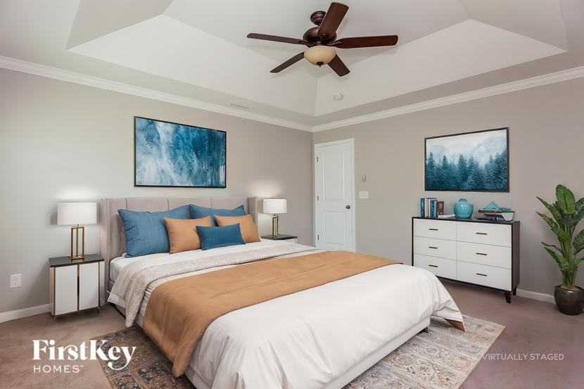 A bedroom with a large bed, a ceiling fan, and a painting on the wall.