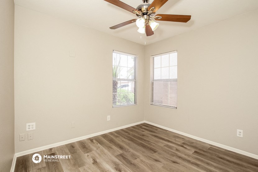 the spacious living room with two windows and a ceiling fan