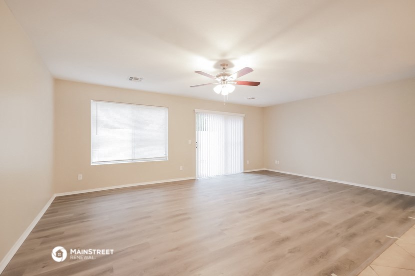 the spacious living room with hardwood floors and a ceiling fan