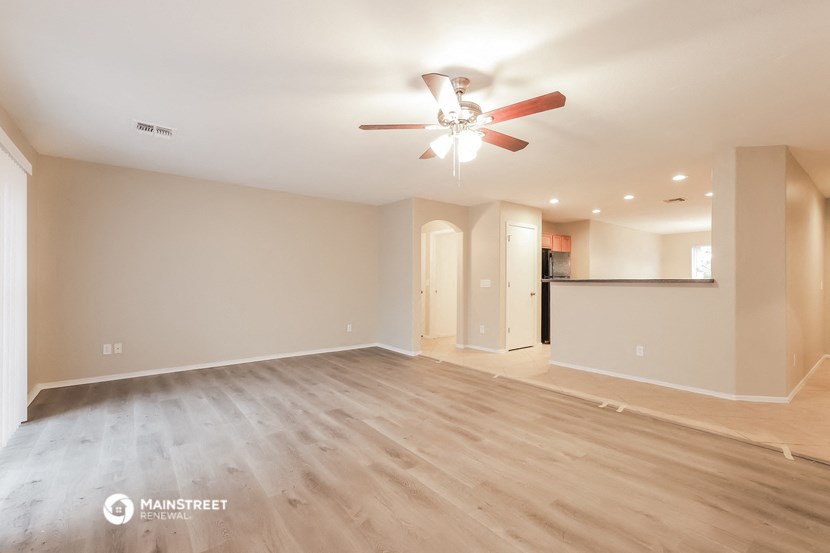 an empty living room with a ceiling fan and a kitchen