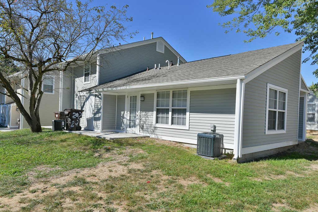 the front of a gray house with a yard and a tree