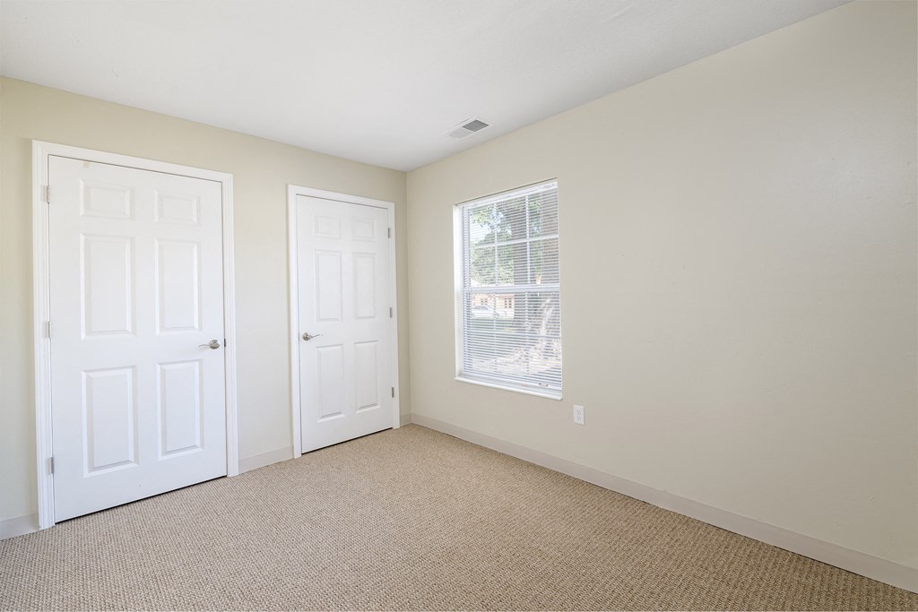 an empty bedroom with two doors and a window