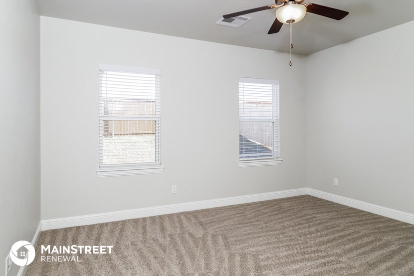 the spacious living room with two windows and a ceiling fan