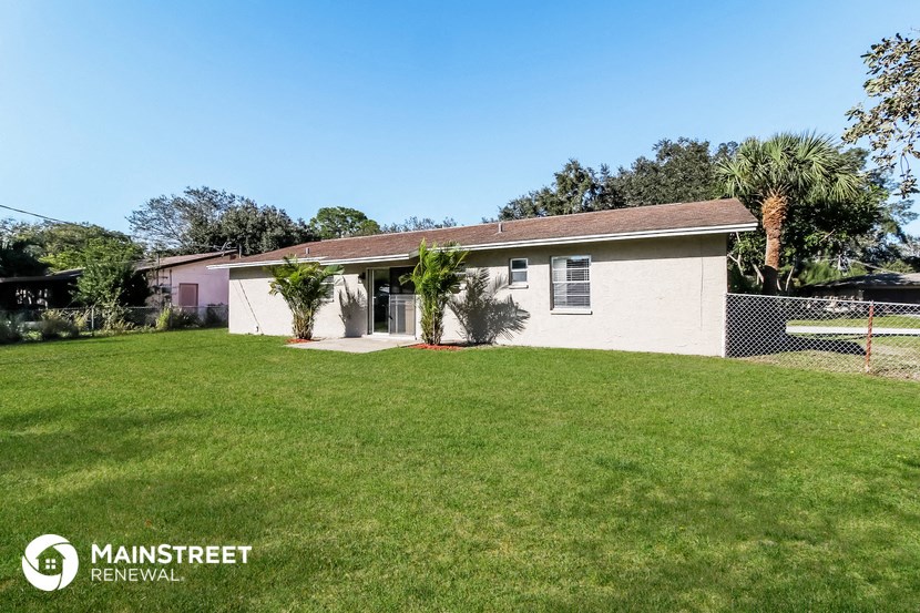 a small white house with a grass yard and palm trees