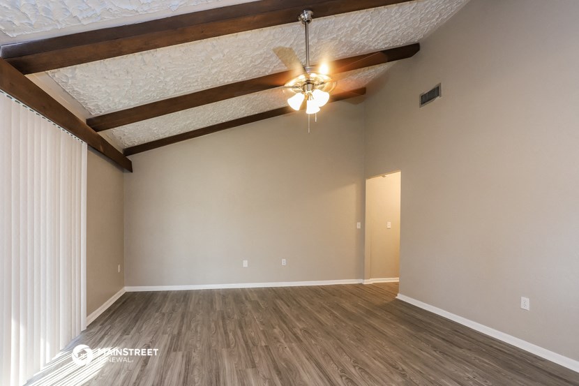 the ceilings in this spacious living room are exposed wood beams and a ceiling fan