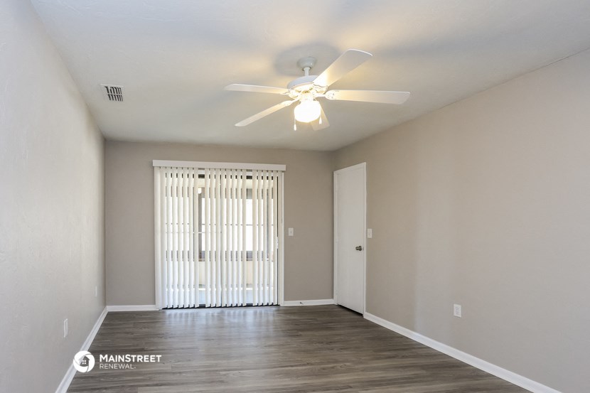 the spacious living room of an apartment with a ceiling fan