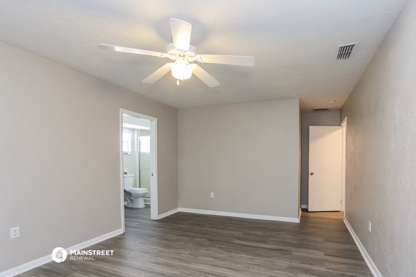 the spacious living room with white walls and a ceiling fan