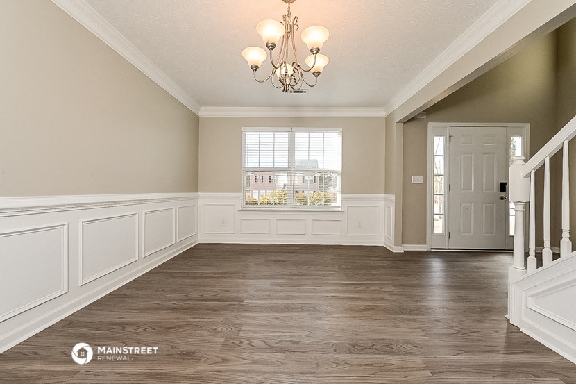 an empty dining room with white wainscoting and a chandelier