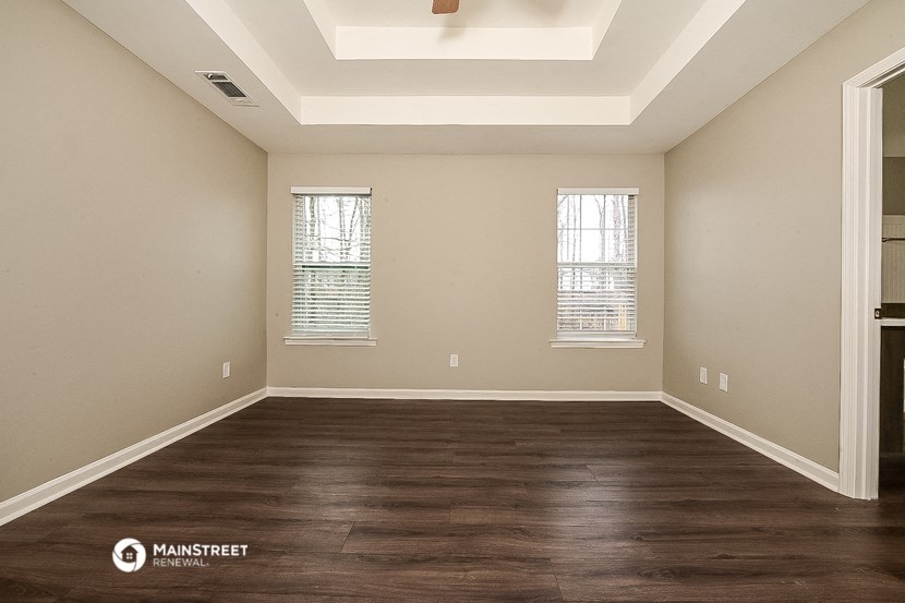 an empty living room with wood flooring and two windows
