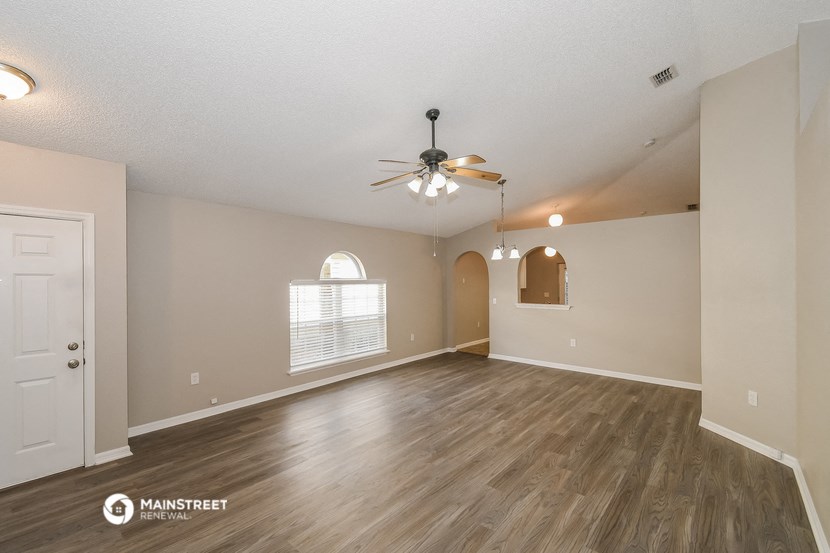 the spacious living room with hardwood flooring and a ceiling fan