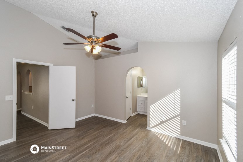 the spacious living room with ceiling fan and hallway to the bathroom