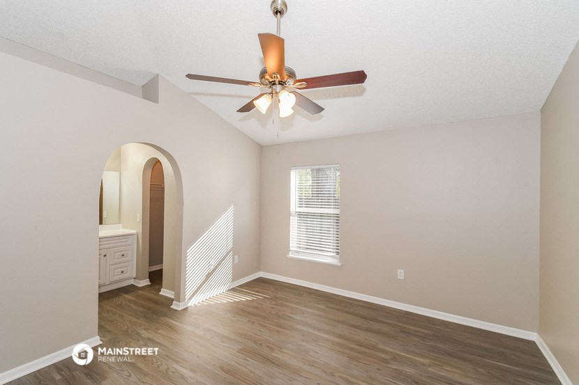 the spacious living room with a ceiling fan and a hallway to the bathroom