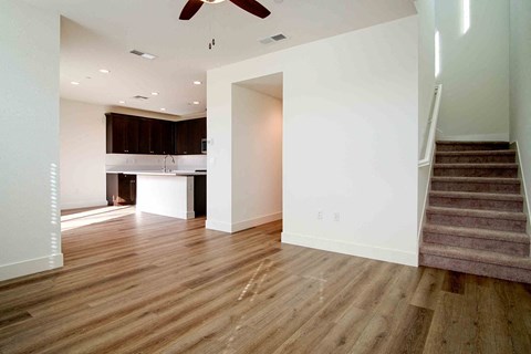 an empty living room with a staircase and a kitchen