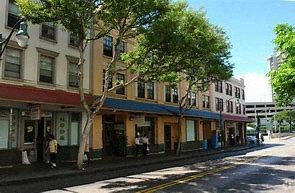 A street view with a building on the left and a tree in the middle.