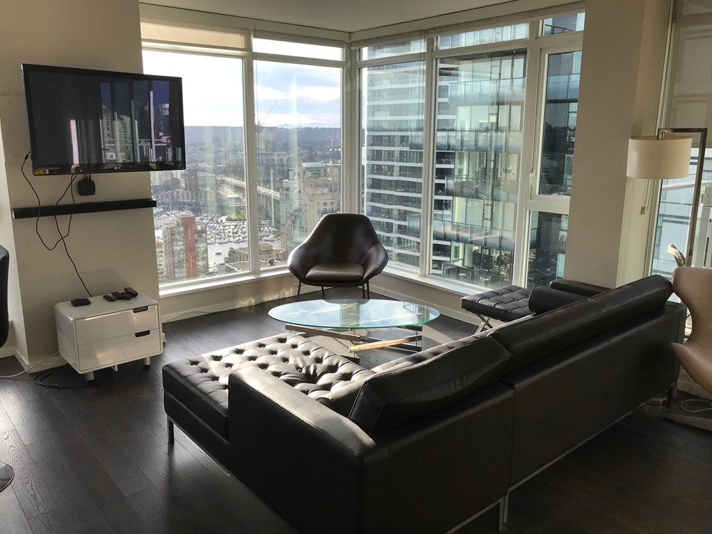 A black couch in a living room with a television and a chair.