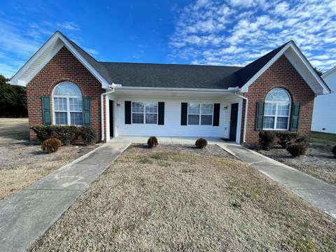 A brick house with a white door and green shutters.
