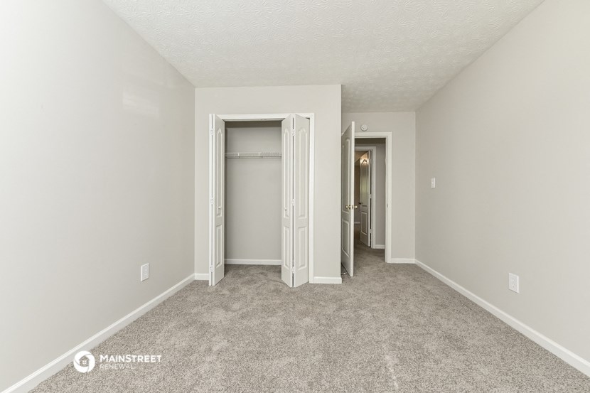 the living room of an apartment with carpet and a hallway to the closet