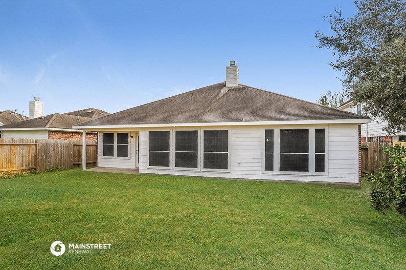 the backyard of a small white house with a lawn and a fence