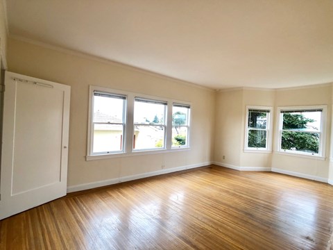 A room with wooden floors and white walls has three windows.