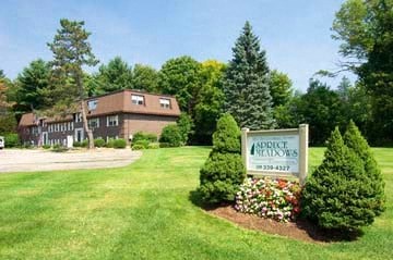 a sign in front of a building with trees and flowers