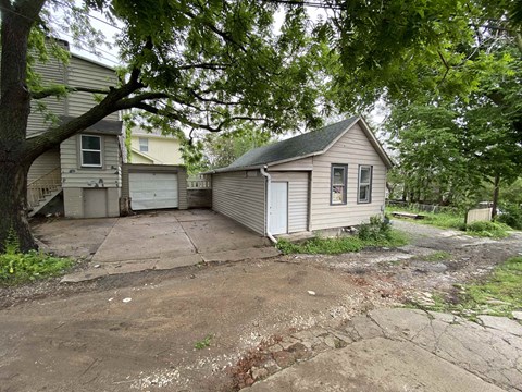 A small house with a garage is surrounded by trees and vegetation.
