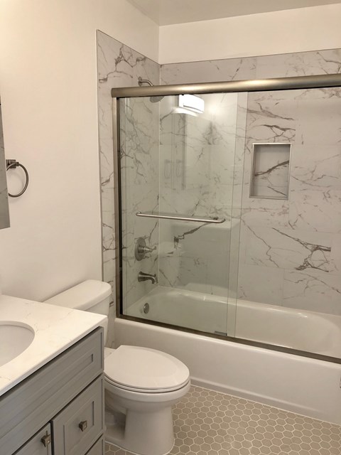 A white toilet sits next to a sink in a marble bathroom.