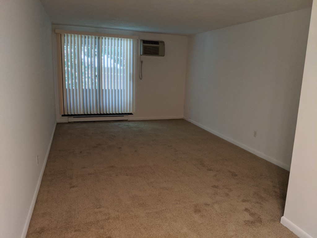 an empty living room with a window and a wall heater