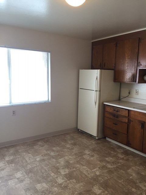 an empty kitchen with a refrigerator and a window