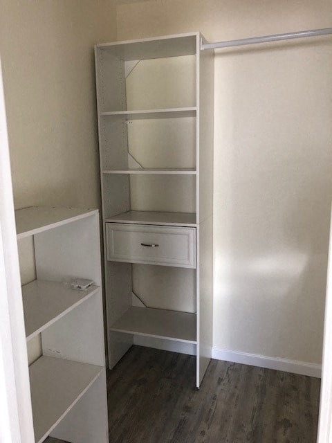 A white shelving unit with a drawer is in a room with white walls.