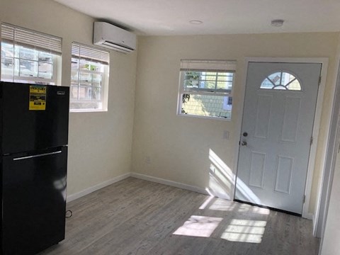A room with a black fridge, a window with blinds, a door and a wall with a window.