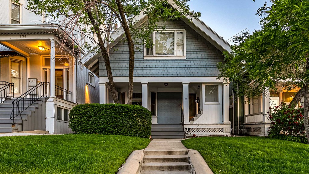 Front exterior view of blue and white First Avenue Home with a bush in front yard