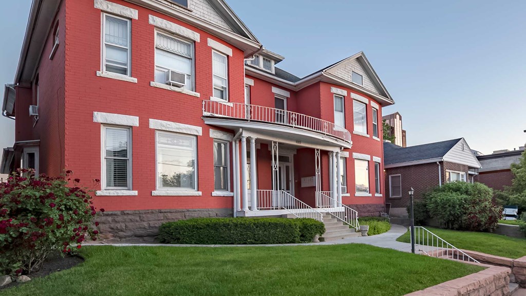 Exterior view of red and white First Avenue Home with bushes in front yard