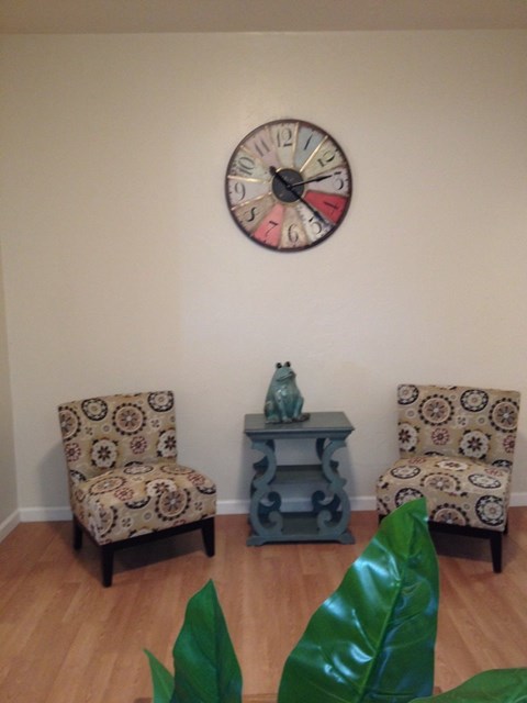 A wall clock hangs above a table with two chairs and a vase on it.