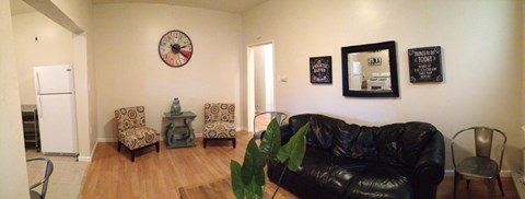 A black leather couch sits in a living room with a clock on the wall.