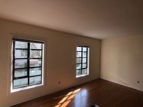 an empty living room with two windows and wooden floors