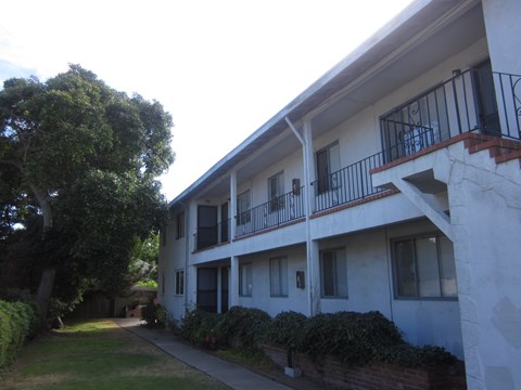 A white building with a balcony and a tree in front of it.