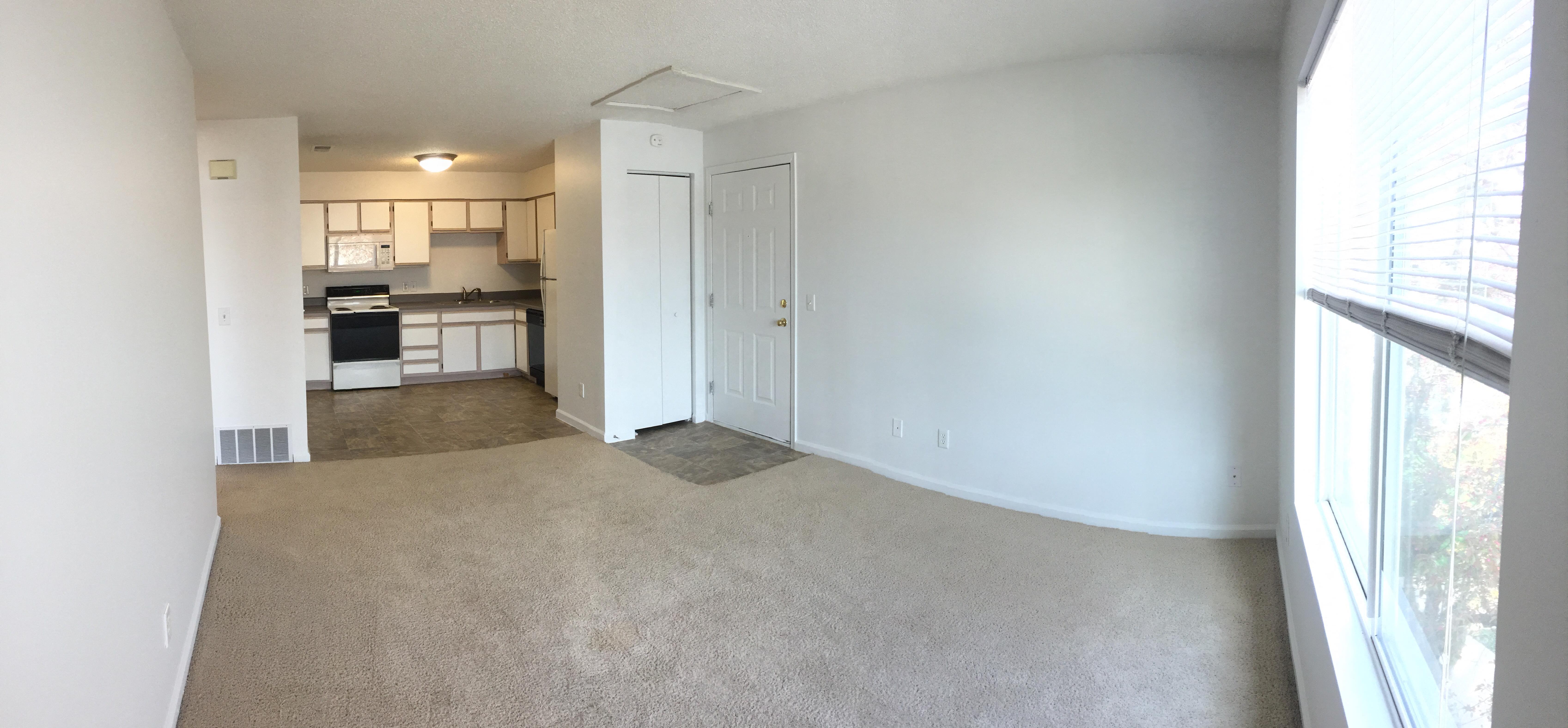 an empty living room with a kitchen in the background