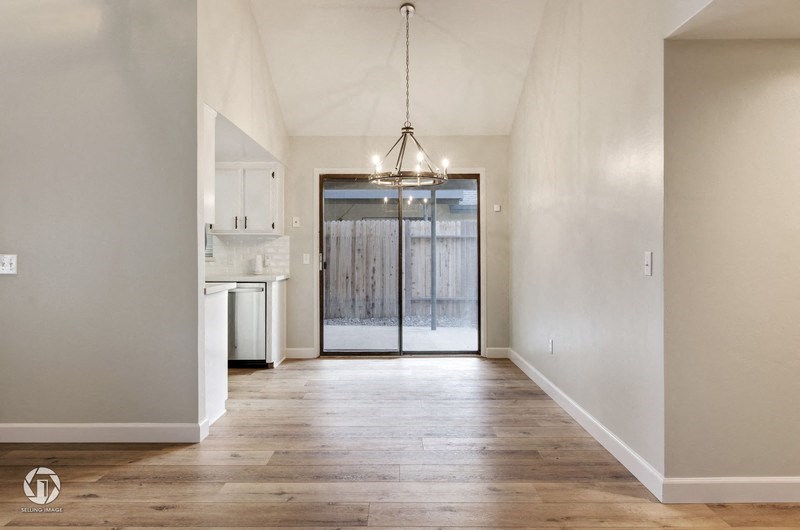 A spacious room with a wooden floor and a chandelier hanging from the ceiling.