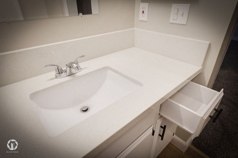 A white bathroom sink with a silver faucet and a white cabinet with a drawer.