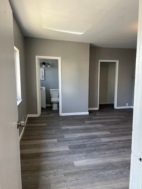 A room with grey walls and wooden flooring with a white door on the left.