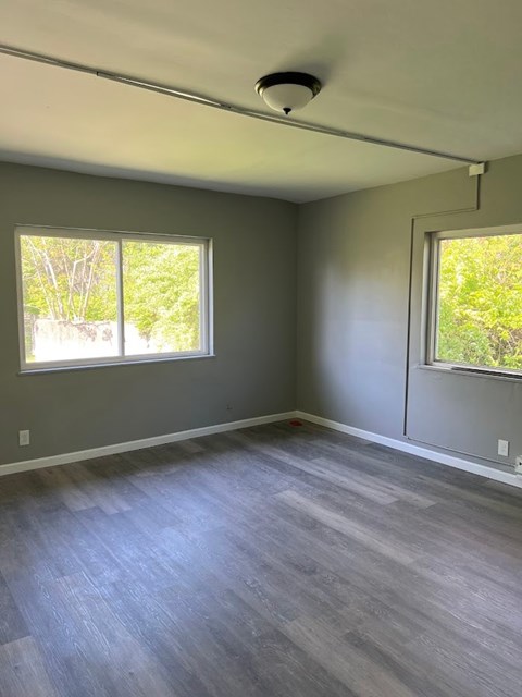 A room with grey flooring and two windows.
