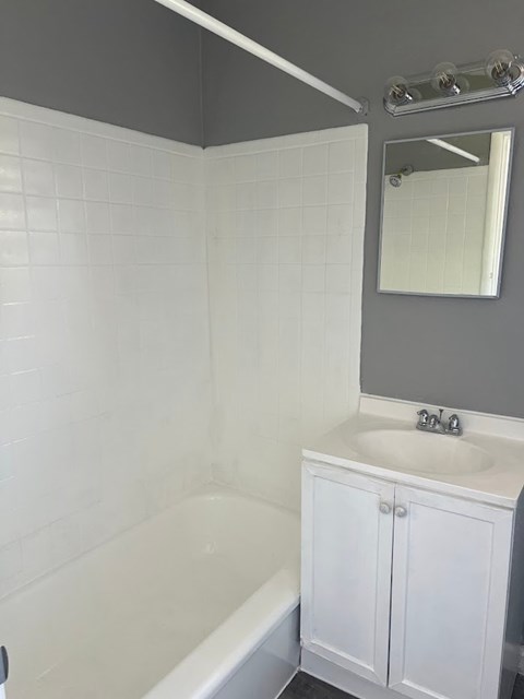 A white bathroom with a white tub, sink, and a mirror.